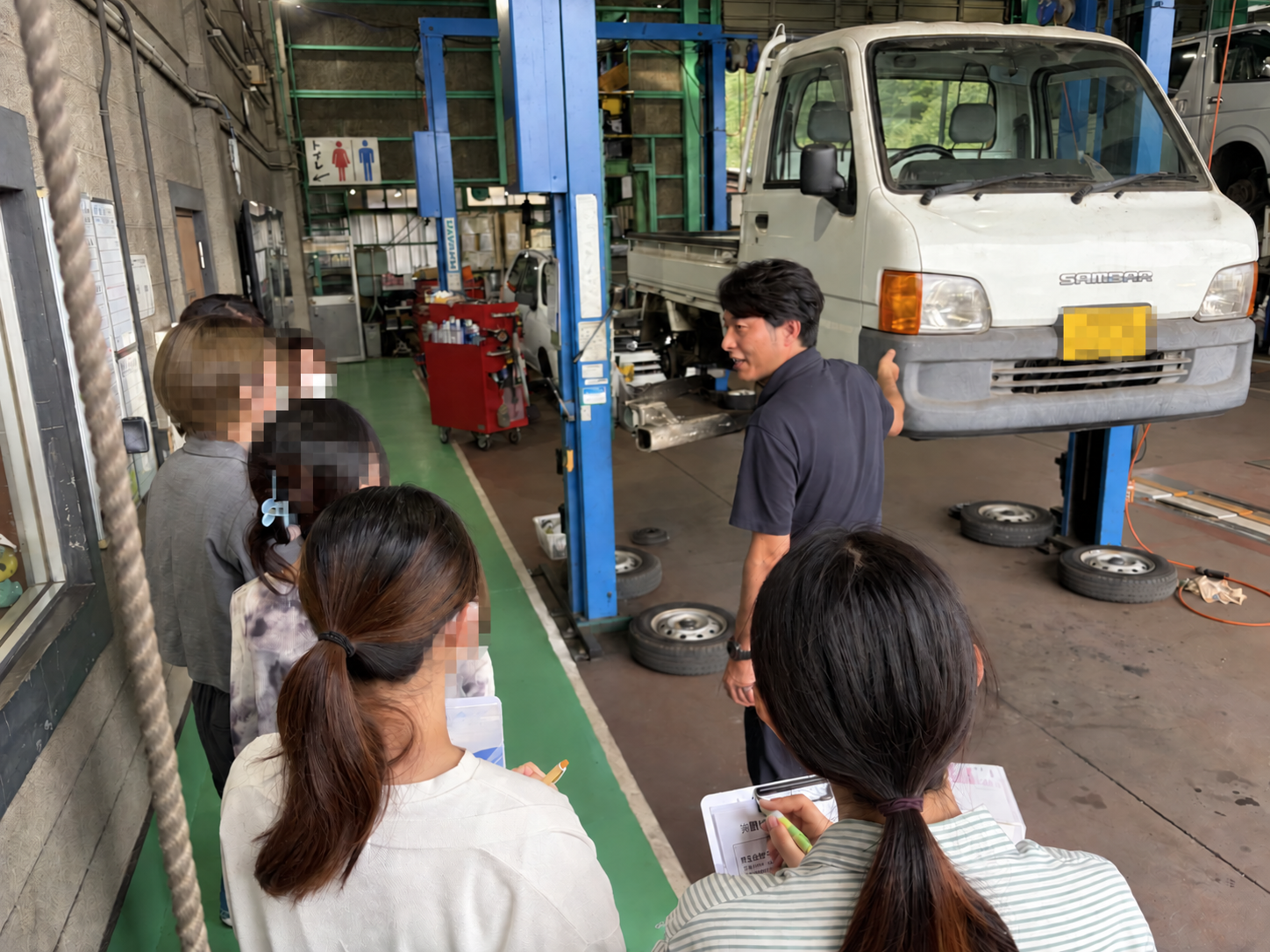 整備工場で、車両を前に整備士の説明を聞く様子